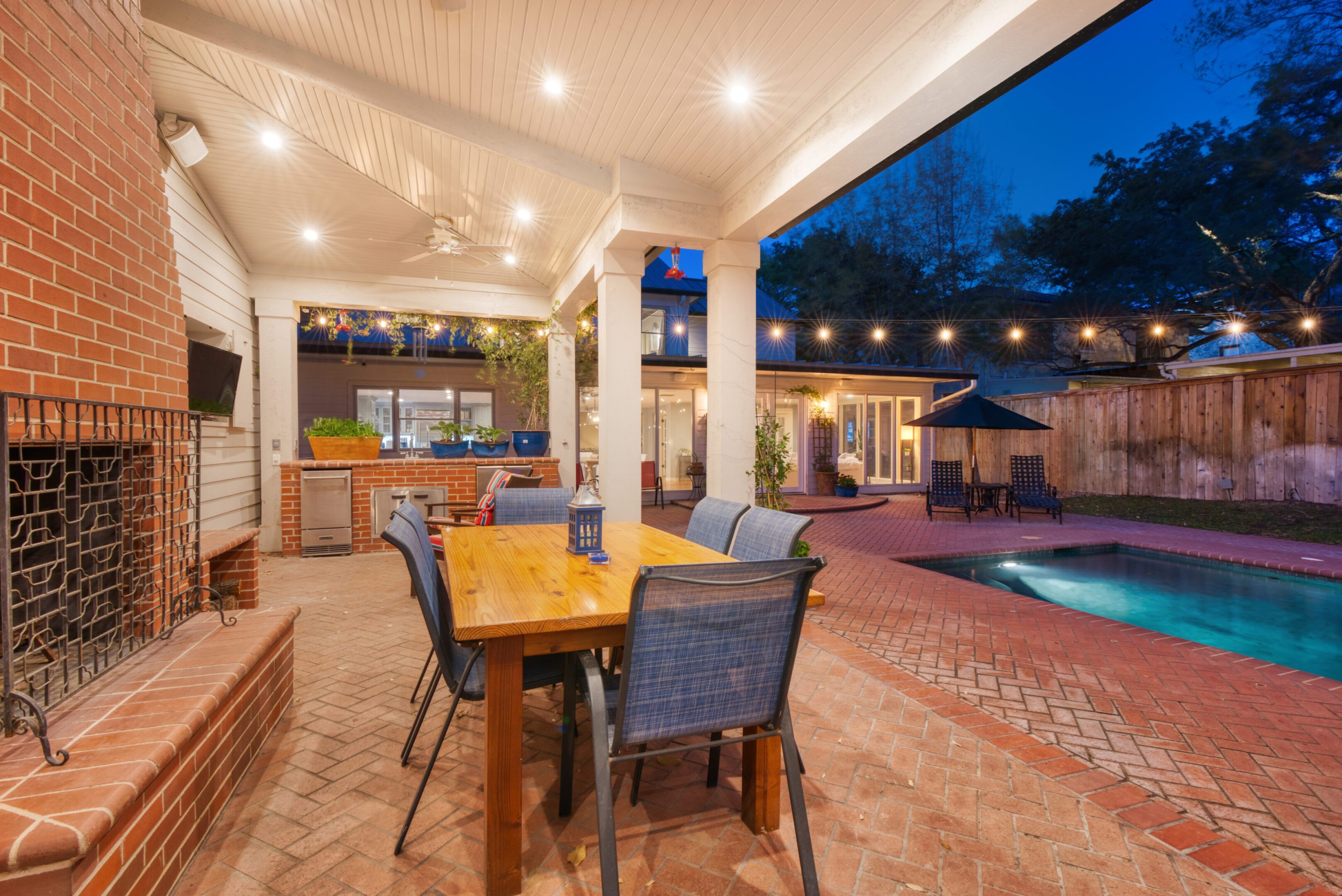 Luxury back porch of an Olmos Park home marketed by Realtor Kerri Hoermann, featuring an outdoor kitchen, fireplace, pool, and outdoor TV.