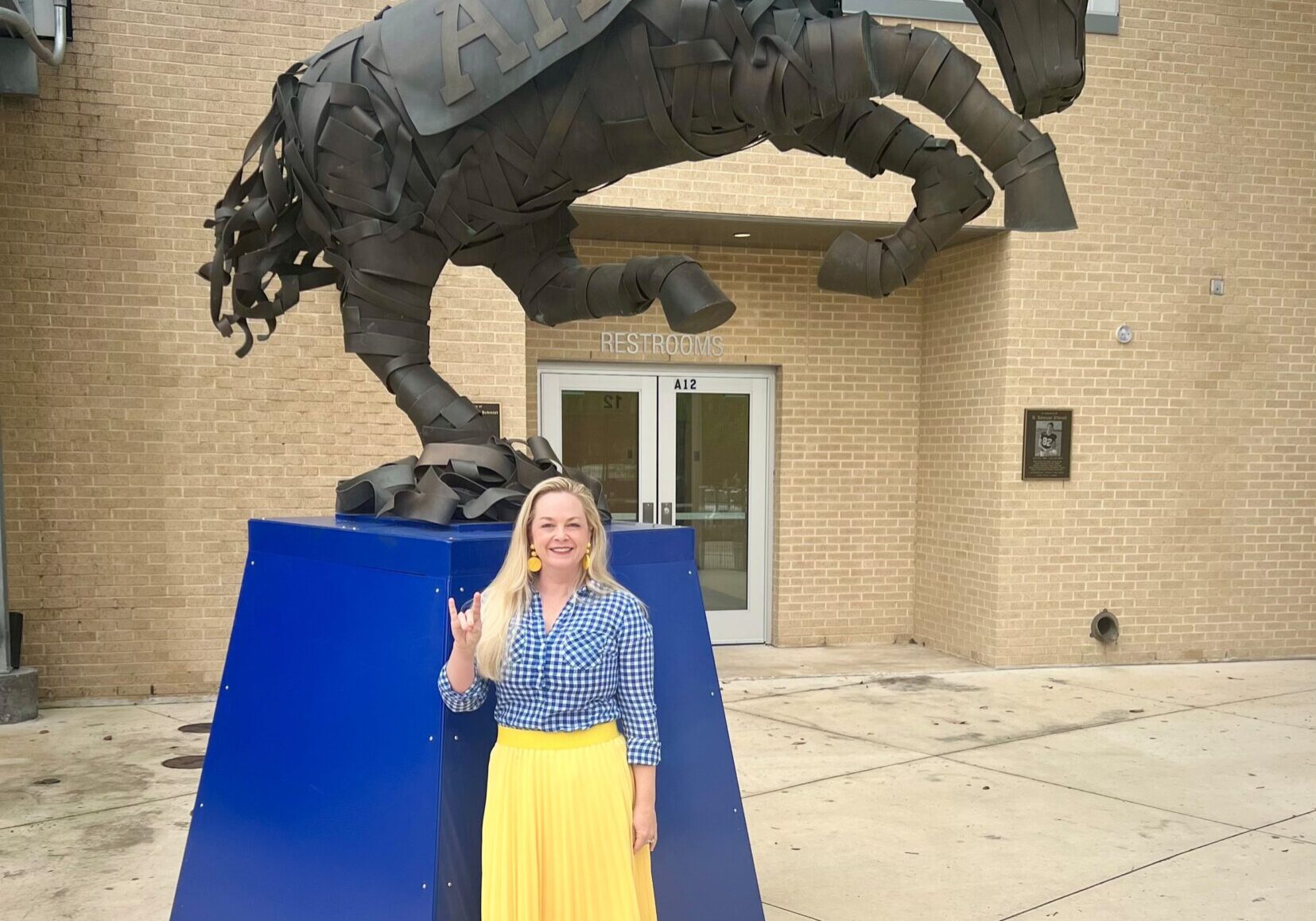 Kerri Hoermann, Alamo Heights Realtor, standing in front of the Alamo Heights High School Mule statue flashing the Mules Up sign.